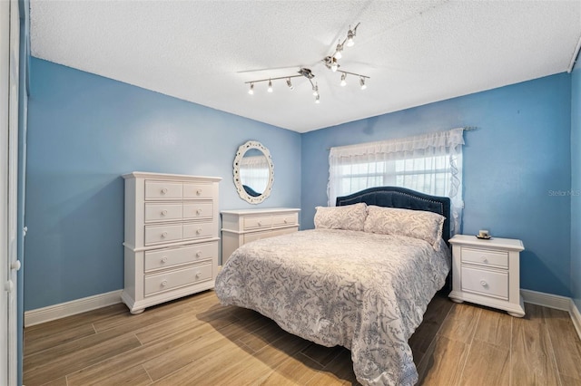 bedroom featuring rail lighting, baseboards, a textured ceiling, and light wood finished floors