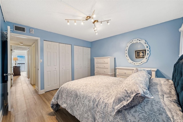 bedroom featuring multiple closets, visible vents, light wood-style floors, a textured ceiling, and baseboards