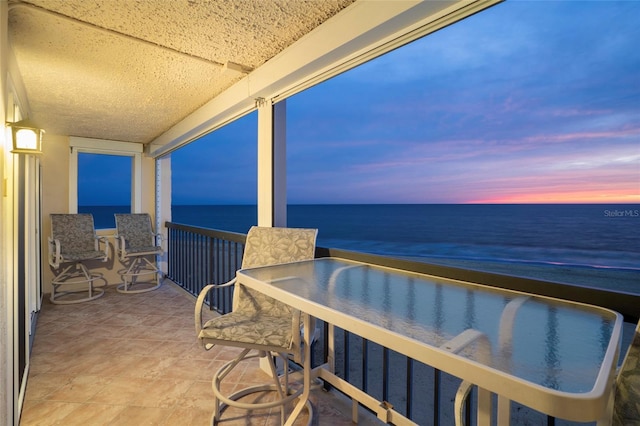 balcony at dusk featuring a water view and a sunroom