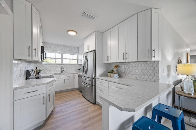 kitchen with kitchen peninsula, stainless steel fridge, tasteful backsplash, white cabinets, and a breakfast bar