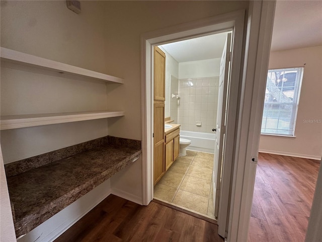 interior space featuring toilet, hardwood / wood-style flooring, tiled shower / bath, and vanity