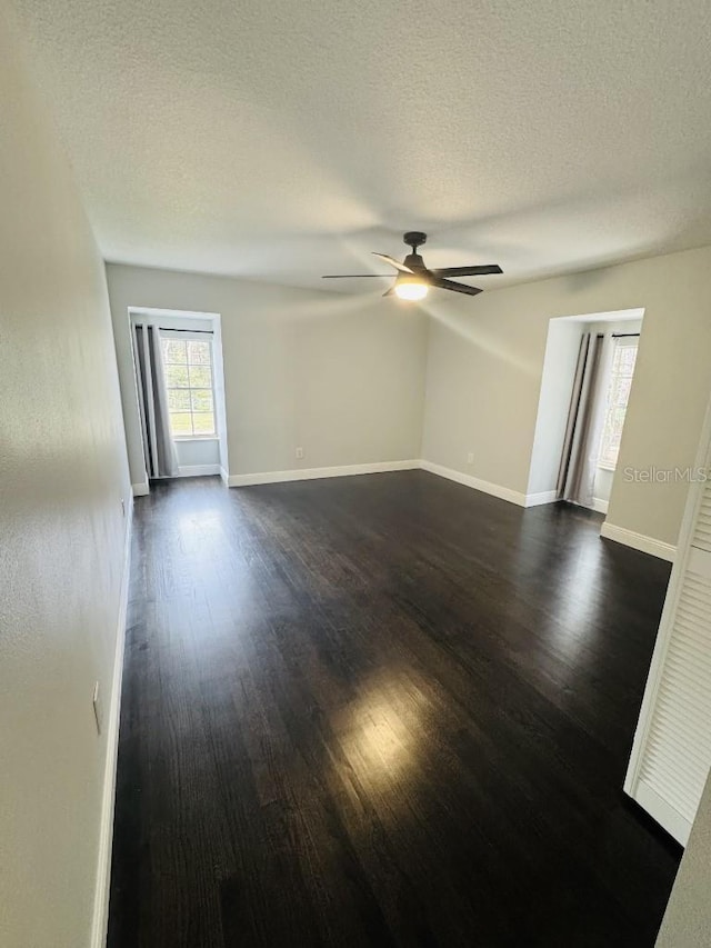 empty room with a textured ceiling, dark wood-type flooring, and ceiling fan