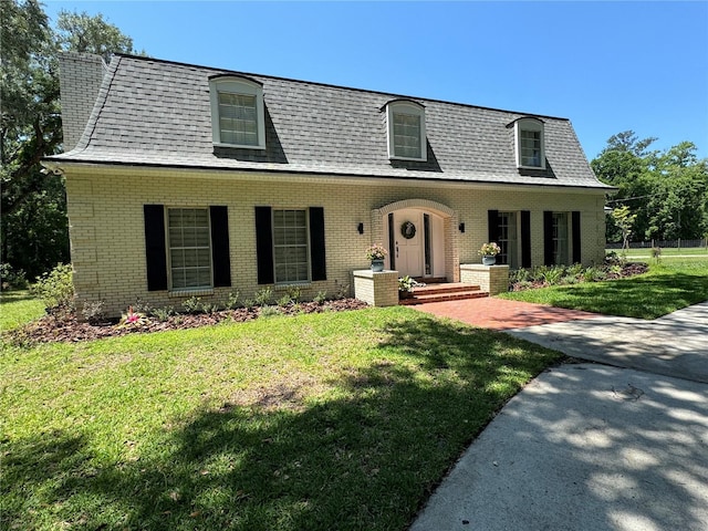 view of front of home featuring a shingled roof, a front yard, and brick siding