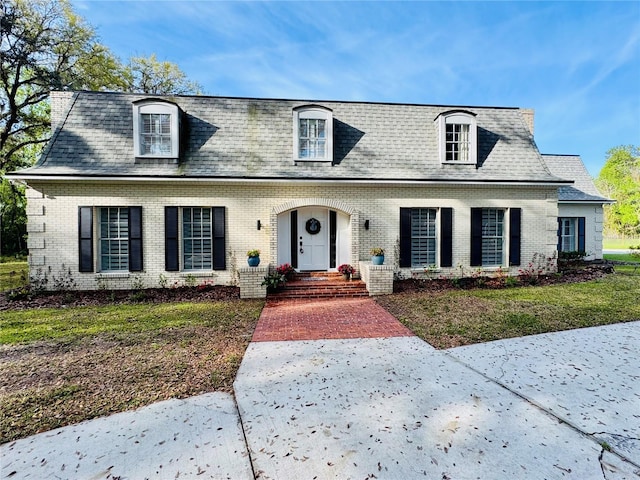 view of front of house with mansard roof, brick siding, and roof with shingles