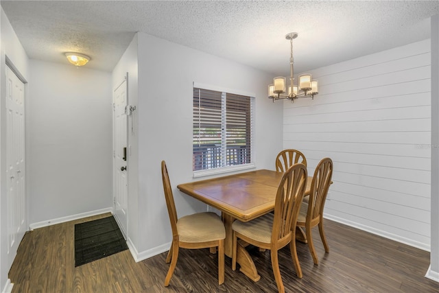 dining space with a chandelier, a textured ceiling, wooden walls, wood finished floors, and baseboards