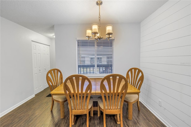 dining room with a textured ceiling, dark wood-type flooring, wood walls, baseboards, and an inviting chandelier