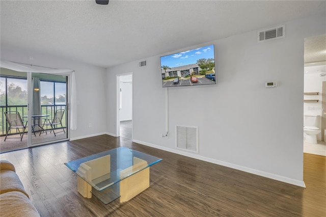 unfurnished living room with a textured ceiling, wood finished floors, visible vents, and baseboards