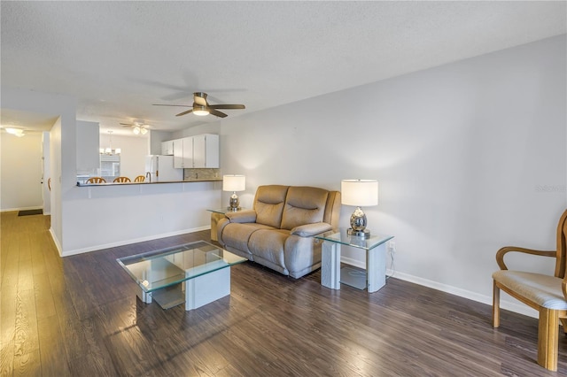 living area featuring baseboards, dark wood finished floors, a textured ceiling, and ceiling fan with notable chandelier