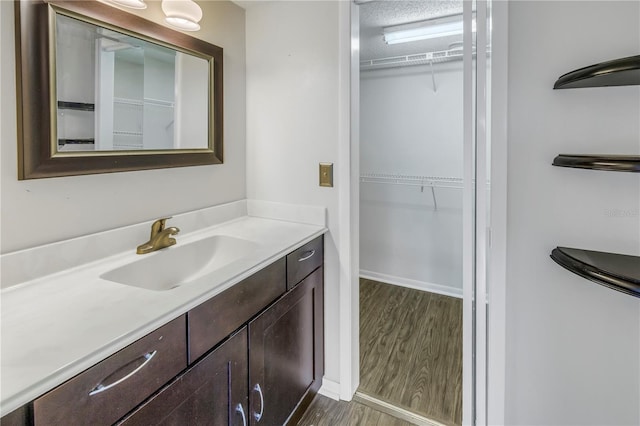 bathroom with a spacious closet, wood finished floors, vanity, and baseboards