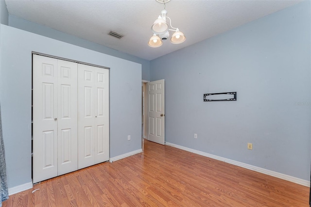 unfurnished bedroom featuring a notable chandelier, light hardwood / wood-style floors, and a closet