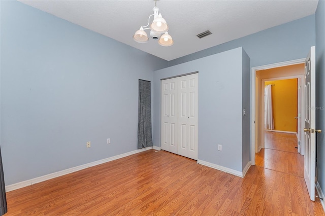 unfurnished bedroom with a closet, light hardwood / wood-style floors, and a notable chandelier