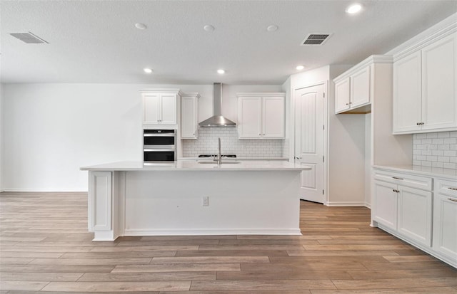 kitchen featuring wall chimney exhaust hood, white cabinetry, and an island with sink