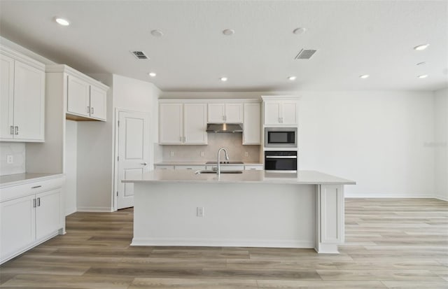 kitchen featuring an island with sink, sink, stainless steel microwave, and oven