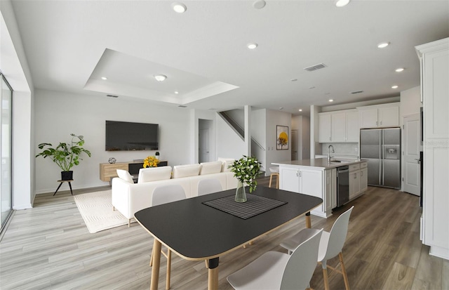 dining space featuring a raised ceiling, sink, and light hardwood / wood-style flooring