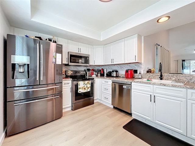 kitchen featuring sink, a raised ceiling, appliances with stainless steel finishes, and white cabinetry