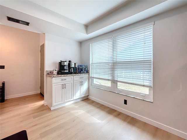 bar featuring light hardwood / wood-style flooring, white cabinetry, and light stone countertops