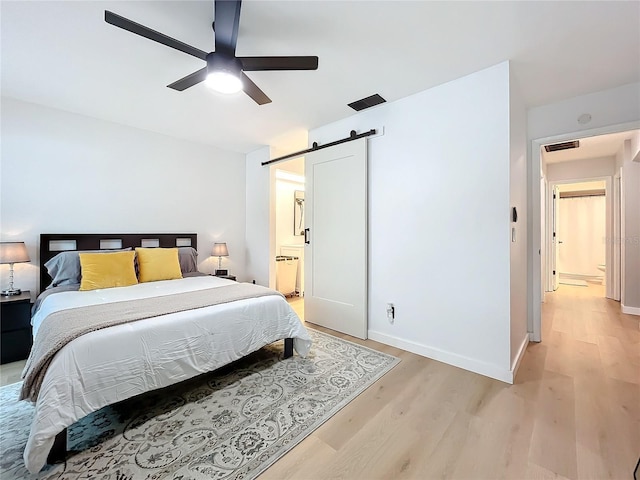 bedroom featuring ensuite bathroom, ceiling fan, a barn door, and light hardwood / wood-style flooring