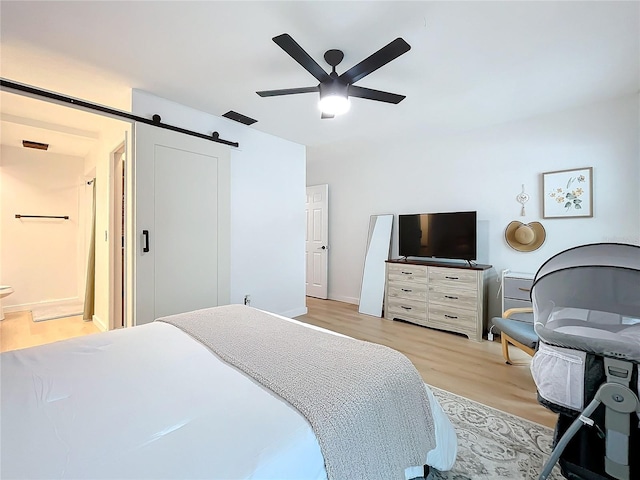 bedroom with ceiling fan, light hardwood / wood-style flooring, connected bathroom, and a barn door