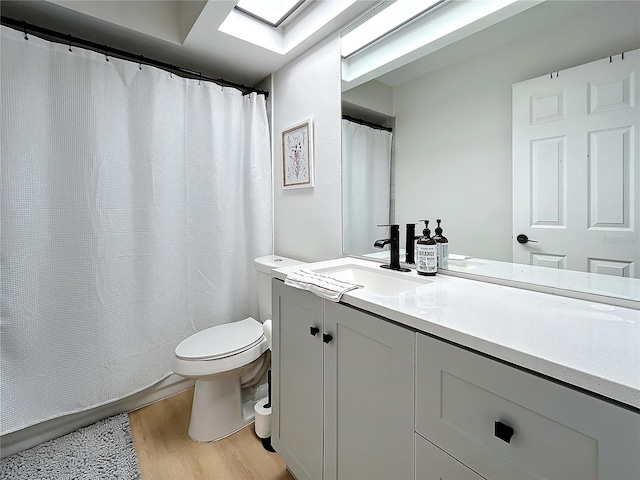 bathroom featuring toilet, hardwood / wood-style flooring, a skylight, and vanity