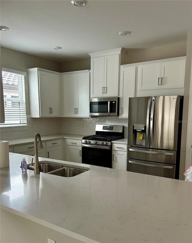 kitchen featuring light stone countertops, appliances with stainless steel finishes, white cabinetry, sink, and backsplash