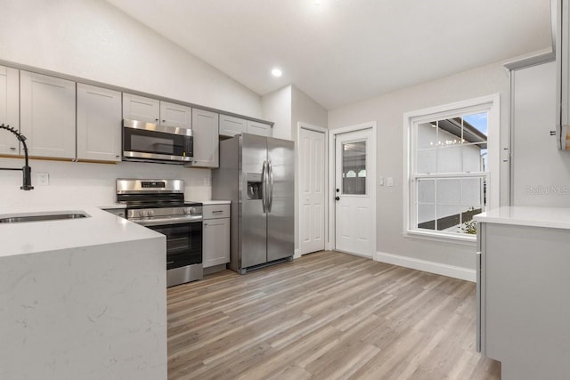 kitchen with vaulted ceiling, light hardwood / wood-style floors, stainless steel appliances, gray cabinetry, and sink