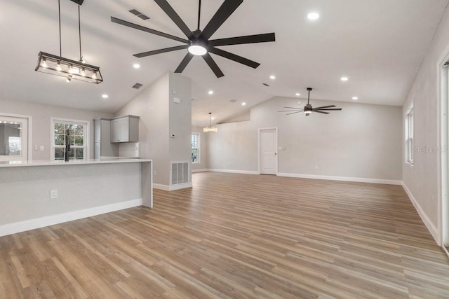 unfurnished living room featuring ceiling fan with notable chandelier, high vaulted ceiling, and light hardwood / wood-style flooring