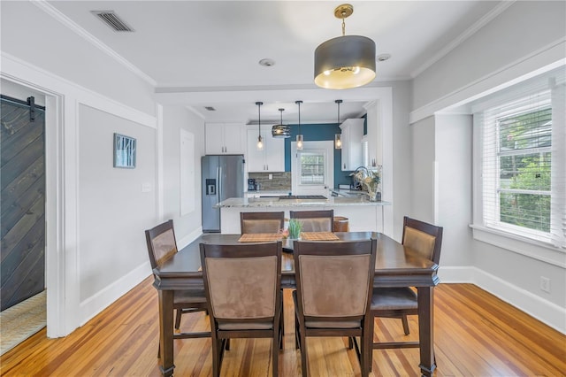 dining area with ornamental molding, light wood-type flooring, and a barn door