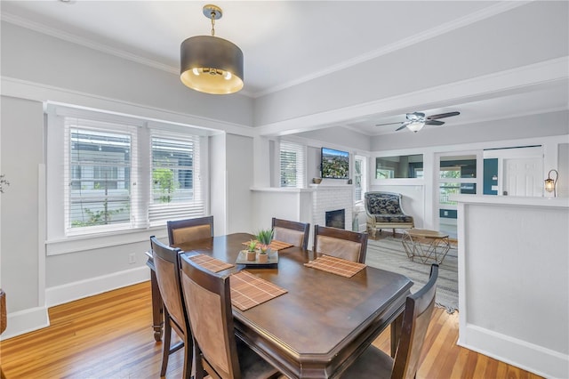 dining area with a brick fireplace, ceiling fan, crown molding, and light hardwood / wood-style floors