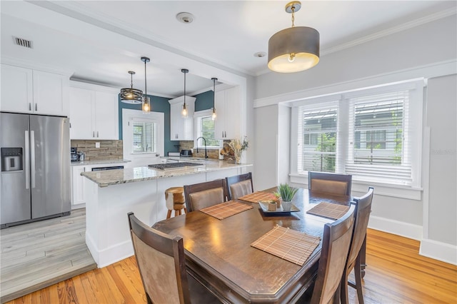 dining area with light wood-type flooring, crown molding, and sink