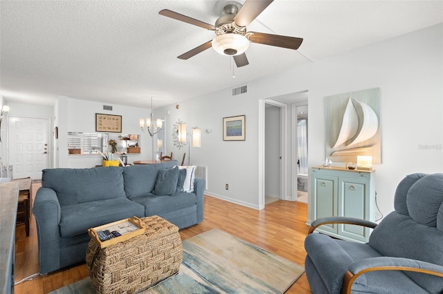 living room with ceiling fan with notable chandelier, a textured ceiling, and light wood-type flooring