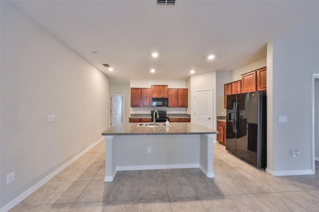 kitchen featuring black appliances, sink, dark stone countertops, a center island with sink, and light tile patterned flooring