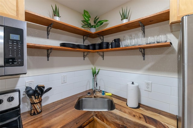 interior space featuring butcher block countertops, sink, decorative backsplash, and appliances with stainless steel finishes