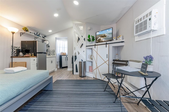 bedroom with lofted ceiling, light hardwood / wood-style flooring, a barn door, and stainless steel refrigerator