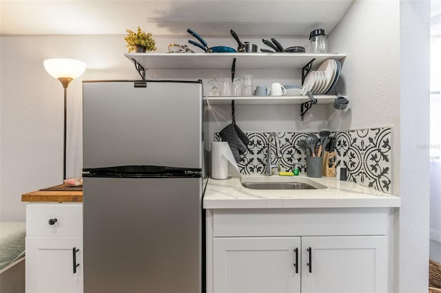 interior space featuring sink, white cabinets, and stainless steel refrigerator