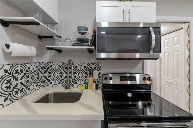 kitchen with white cabinetry, stainless steel appliances, light stone countertops, and sink