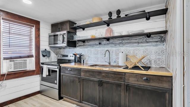 kitchen with dark brown cabinetry, sink, tasteful backsplash, light wood-type flooring, and stainless steel appliances