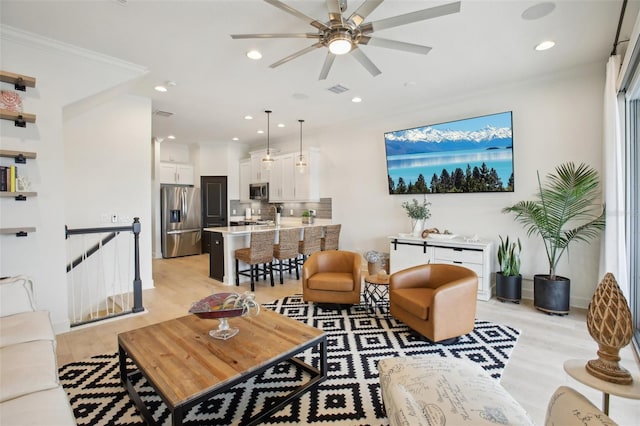 living room with ceiling fan, light wood-type flooring, and ornamental molding