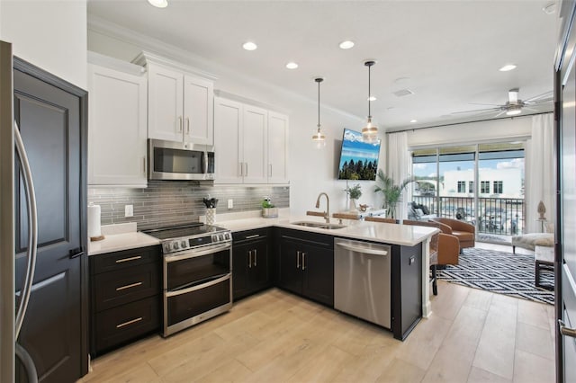 kitchen featuring kitchen peninsula, appliances with stainless steel finishes, decorative light fixtures, white cabinets, and sink