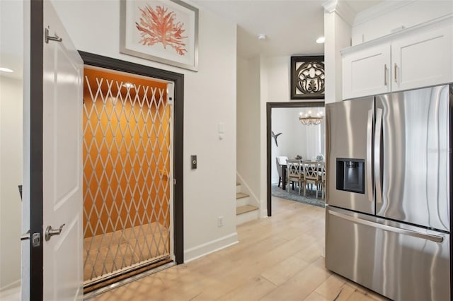 kitchen with stainless steel refrigerator with ice dispenser, white cabinetry, an inviting chandelier, light hardwood / wood-style flooring, and crown molding