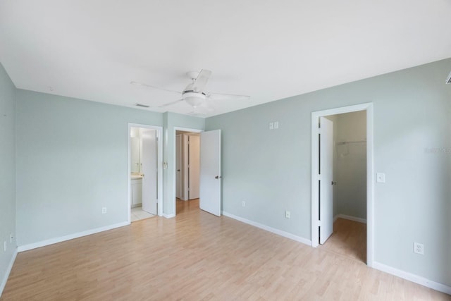 unfurnished bedroom with a walk in closet, connected bathroom, a closet, ceiling fan, and light hardwood / wood-style flooring