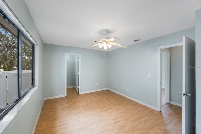 unfurnished bedroom with ceiling fan, light wood-type flooring, a spacious closet, and a closet