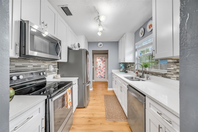 kitchen with light hardwood / wood-style floors, stainless steel appliances, sink, white cabinetry, and tasteful backsplash