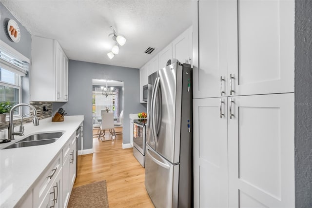 kitchen with white cabinets, light hardwood / wood-style floors, stainless steel appliances, a textured ceiling, and sink