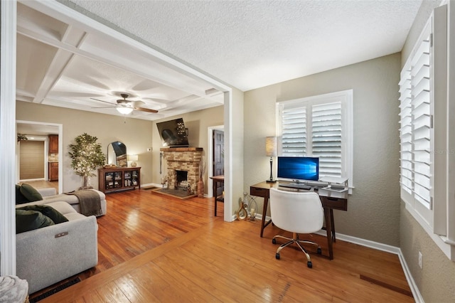 home office with a textured ceiling, a stone fireplace, ceiling fan, hardwood / wood-style flooring, and beam ceiling