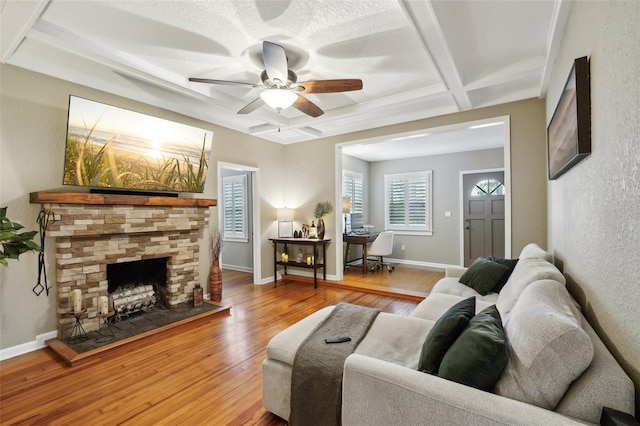 living room with hardwood / wood-style floors, coffered ceiling, a stone fireplace, ceiling fan, and beam ceiling