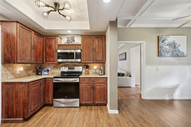 kitchen with light hardwood / wood-style floors, ceiling fan, appliances with stainless steel finishes, decorative backsplash, and light stone countertops