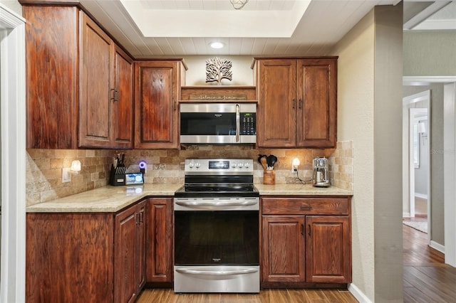 kitchen featuring a raised ceiling, decorative backsplash, light wood-type flooring, light stone countertops, and stainless steel appliances