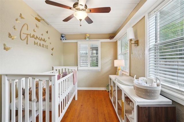 bedroom with ceiling fan, a nursery area, wooden ceiling, and wood-type flooring