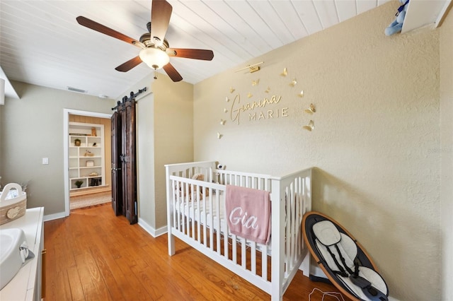 bedroom featuring ceiling fan, a barn door, a nursery area, and hardwood / wood-style flooring