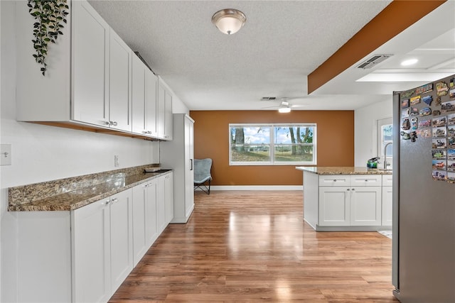 kitchen featuring light stone countertops, white cabinetry, stainless steel refrigerator, kitchen peninsula, and light wood-type flooring